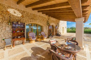 A covered patio area with stone walls, wicker furniture, and a stone floor. - Na Pont - Villa With Private Pool In Campos (Campos, Illes Balears)