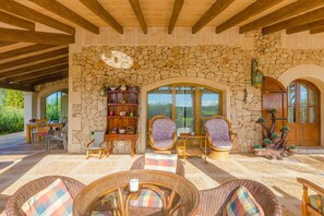 A covered outdoor seating area with stone walls, wicker furniture, and a stone fireplace. - Na Pont - Villa With Private Pool In Campos (Campos, Illes Balears)