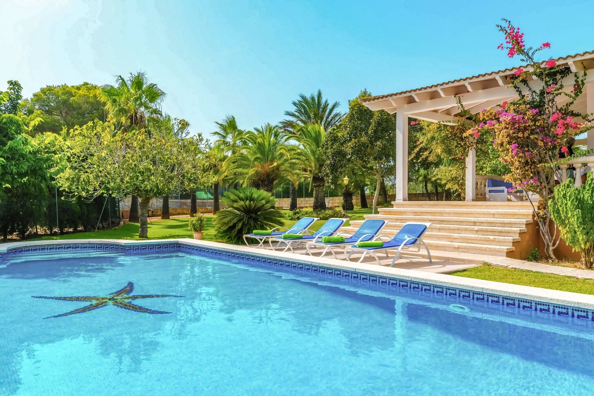 A swimming pool with a starfish design, surrounded by blue lounge chairs and a pergola with pink flowers.