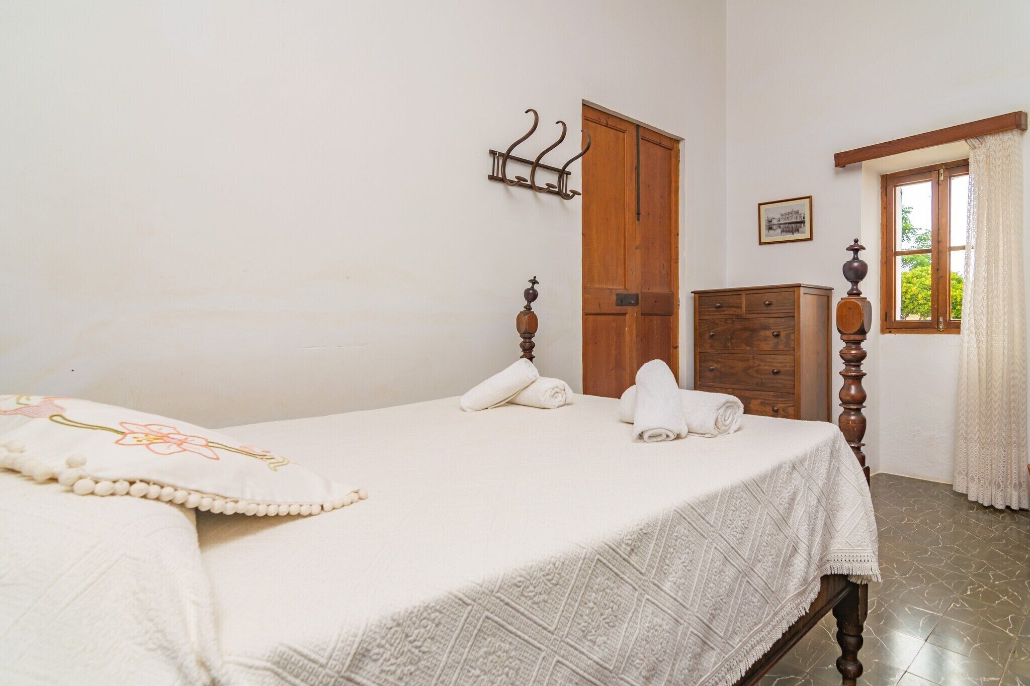 Un letto rifatto con lenzuola bianche e un cuscino decorativo, un armadio in legno e una finestra con tende.