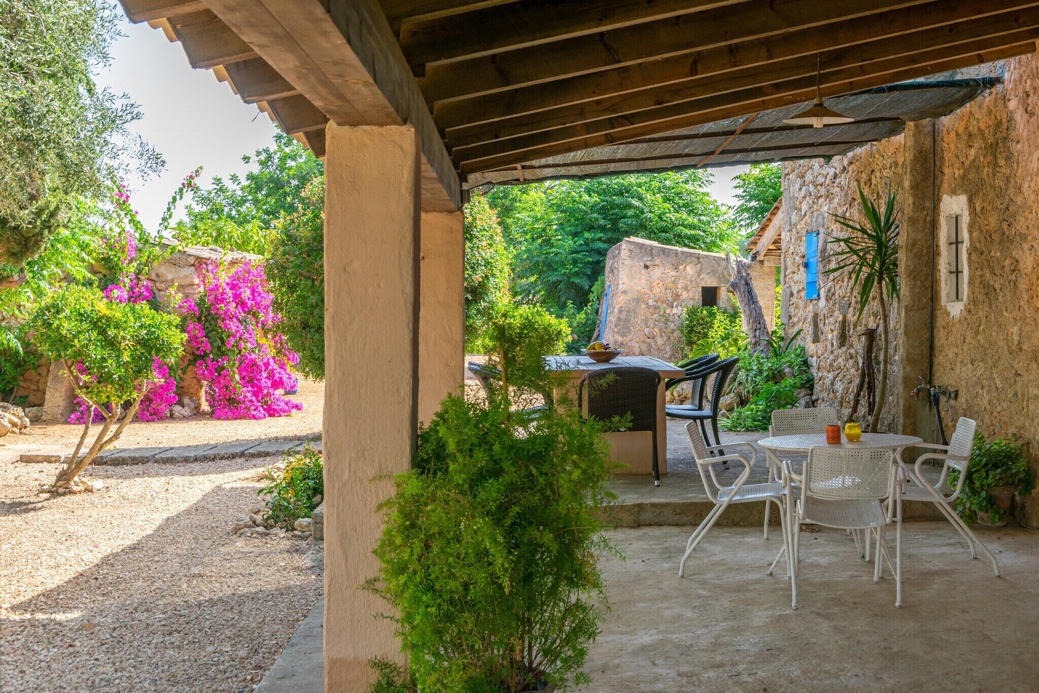 Un patio al aire libre con una mesa y sillas, rodeado de follaje y un muro de piedra.