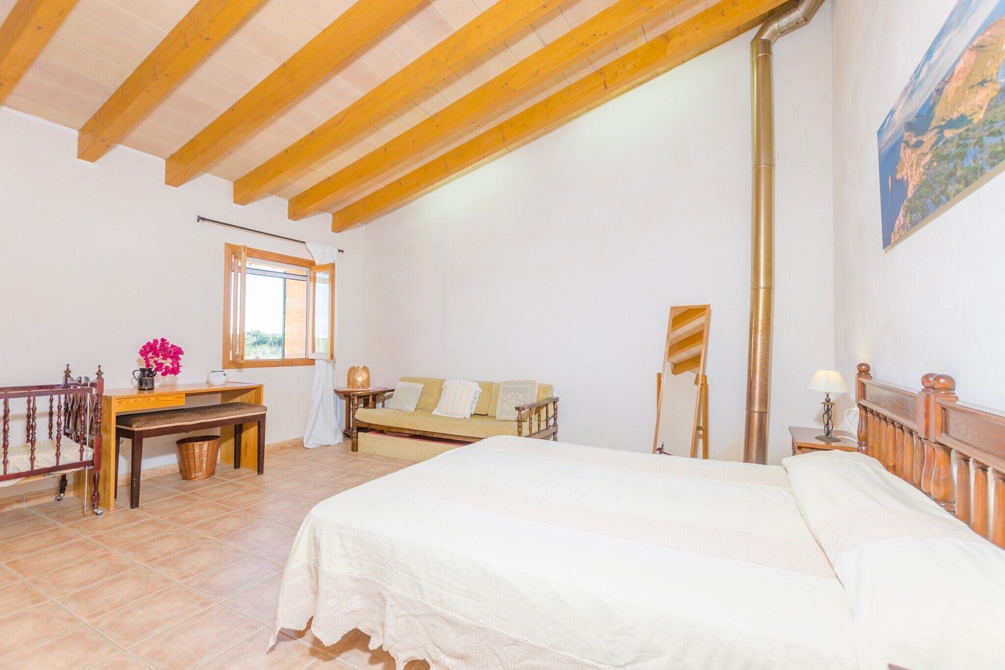 A bedroom with a wooden ceiling, a bed, a desk, a chair, a window, and a painting on the wall.