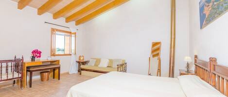 A bedroom with a wooden ceiling, a bed, a desk, a chair, a window, and a painting on the wall.