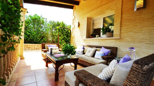An outdoor living area with a wicker sofa, a wooden coffee table, and a stone wall.