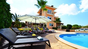 A poolside area with lounge chairs and umbrellas, a pool, and a multi-story building with balconies.