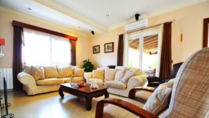 A living room with two sofas, a coffee table, and a chair. There is a window with curtains, a plant, and a picture on the wall.