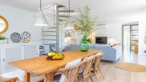 Ein modernes Wohnzimmer mit einem Holzesstisch, Korbstühlen, einem blauen Sofa und einem Fernseher.