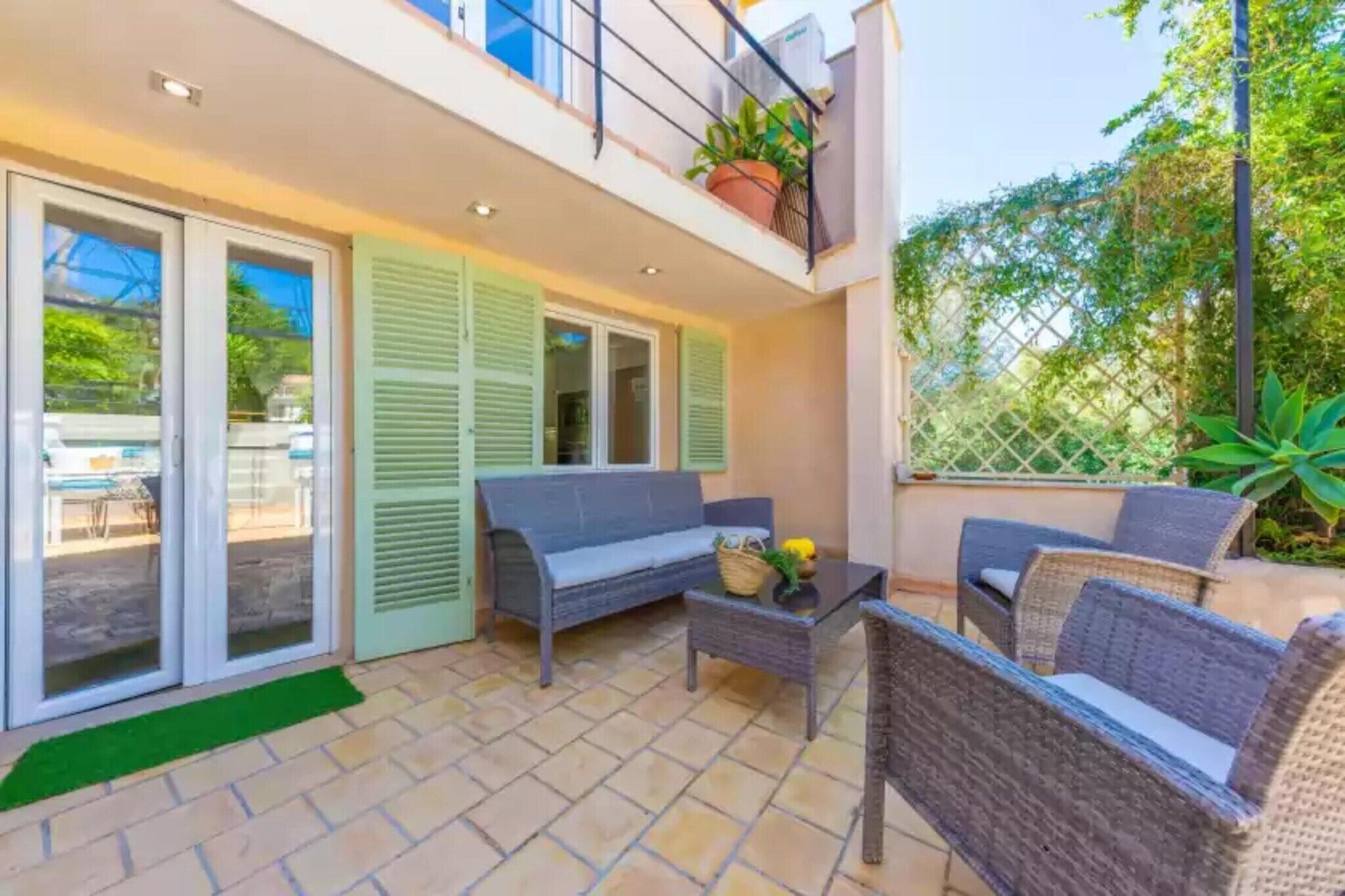 A balcony with wicker furniture, a table with a basket and flowers, and a view of the garden.