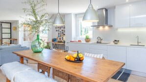 Eine moderne Küche mit weißen Schränken, einem Holztisch mit Obstschale und Pendelleuchten.