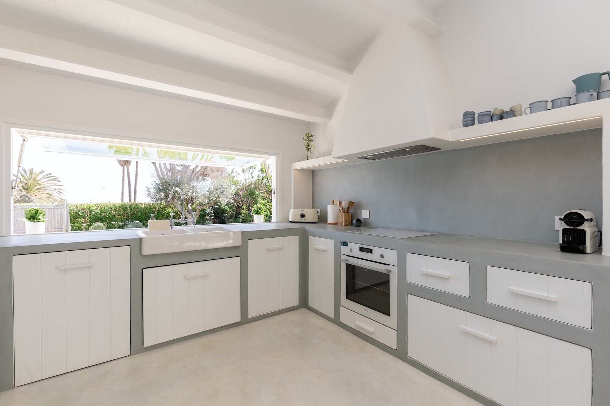 A modern kitchen with white cabinets, a built-in oven, and a window overlooking greenery.