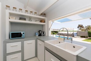 Enjoy a kitchen with a microwave and kettle, white sink, and cabinetry, offering a view of the pool and outdoor furniture.