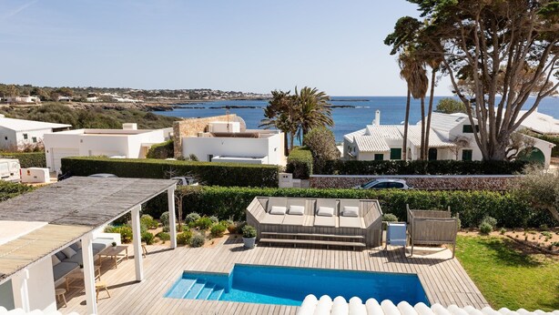 A pool area with a view of the sea, a wooden deck, and a white building with a balcony. - Sa Blava - Villa With Private Pool. Free Wifi (, Illes Balears)