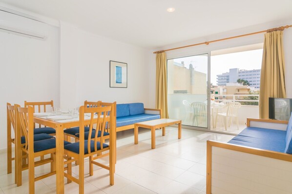 A modern living room with a dining table, blue sofa, and a TV. - Massanet (ba) - Apartment In Canyamel. Free Wifi (Canyamel, Illes Balears)