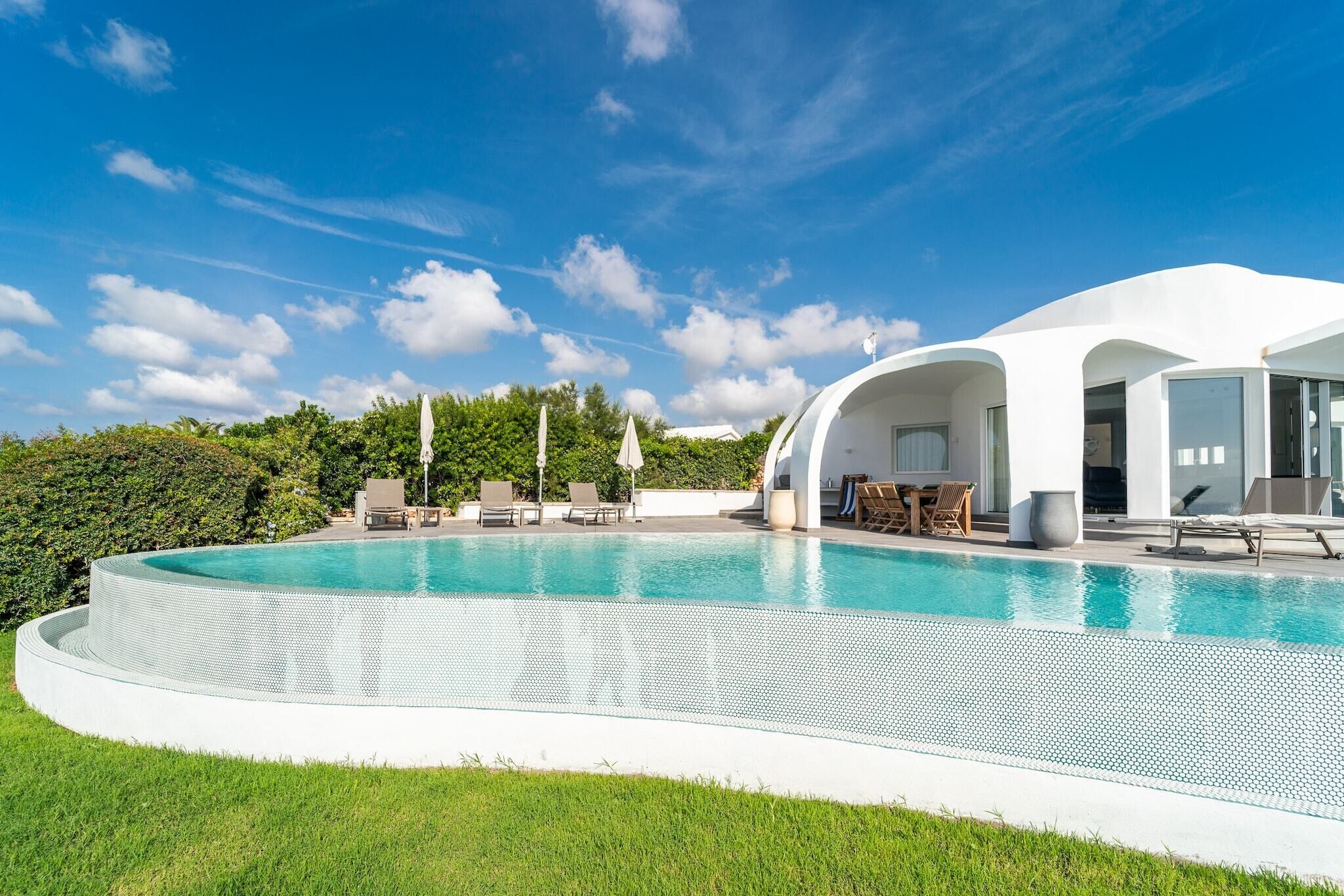 A modern house with a large swimming pool, outdoor seating, and a lush green landscape.