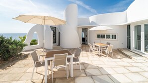 Une terrasse extérieure moderne, avec des meubles blancs et des parasols, offrant une vue imprenable sur l’océan.
