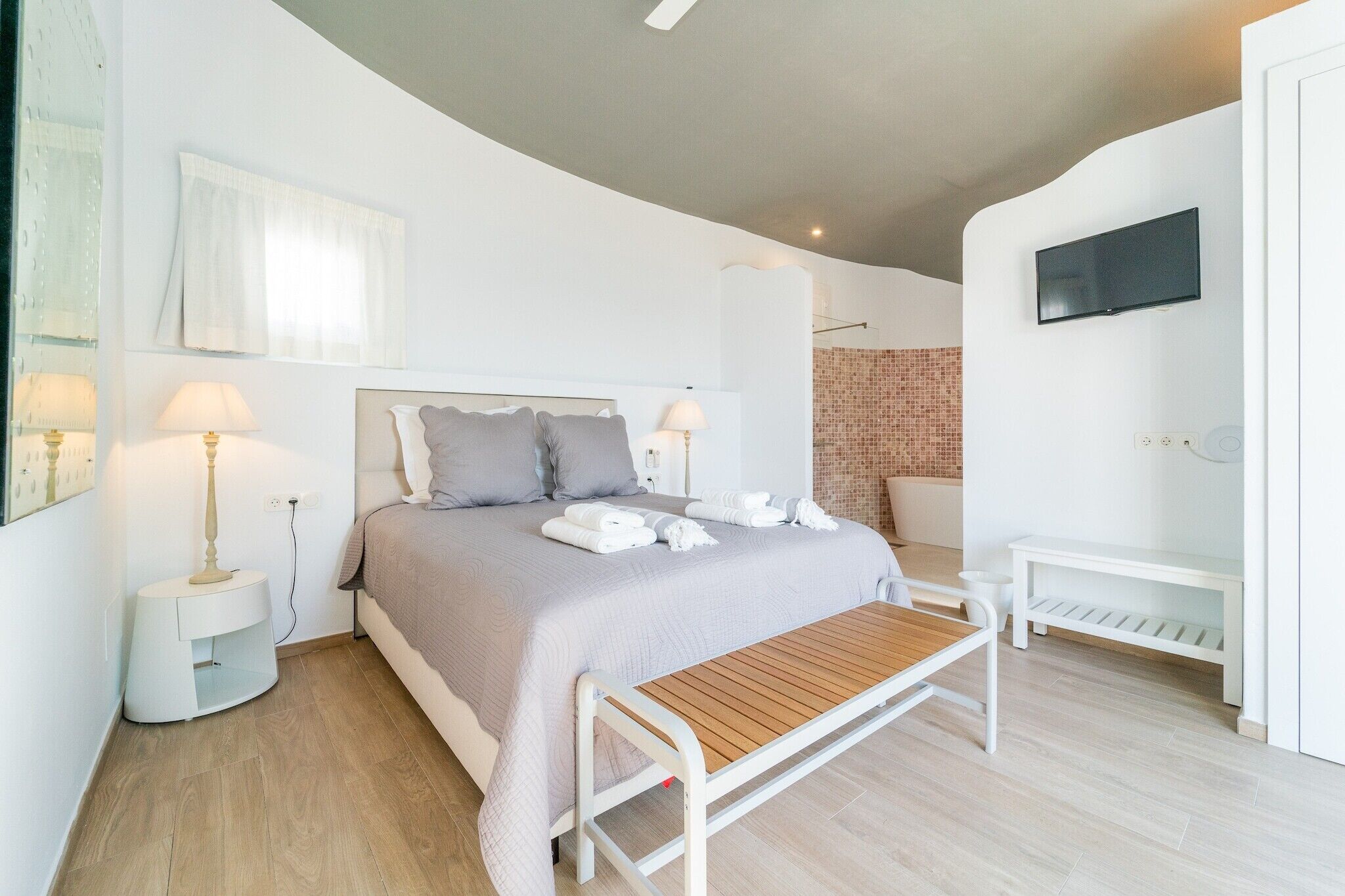 A bedroom with a bed, bedside lamps, a TV, and a bench.