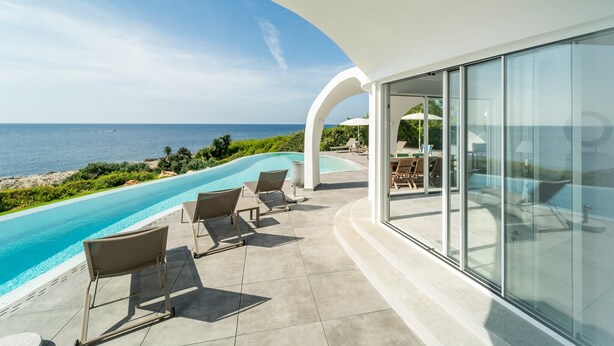 Un espace piscine extérieur moderne, avec une eau d’un bleu limpide, entouré de chaises longues et offrant une vue sur une plage avec l’océan en toile de fond.