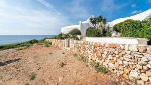 Une propriété située sur la côte, avec un mur en pierre, un bâtiment blanc et des palmiers.
