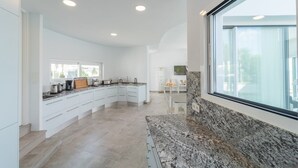 Une cuisine moderne avec des meubles blancs, des plans de travail en granit et une grande fenêtre qui laisse entrer la lumière naturelle.