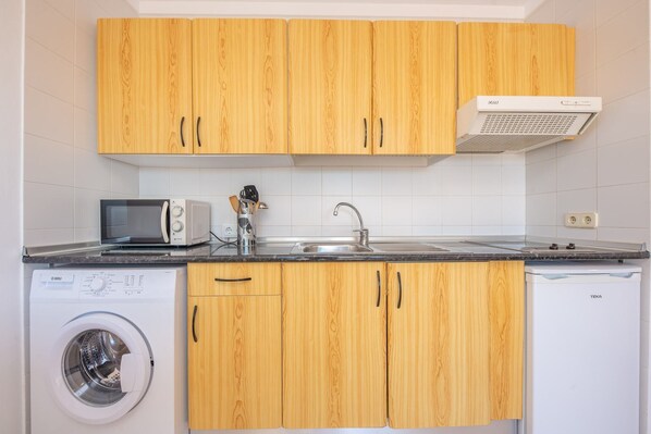 A compact kitchen with wooden cabinets, a washing machine, a microwave, and a dishwasher.