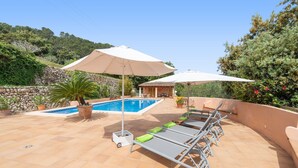 A rooftop pool area with lounge chairs and umbrellas, surrounded by stone walls and greenery.