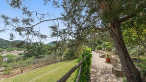 A stone pathway leading through a garden with a view of a distant village and hills.