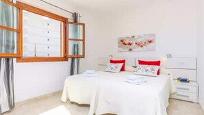 A bedroom with two beds, a window, a nightstand, and a wall-mounted artwork.