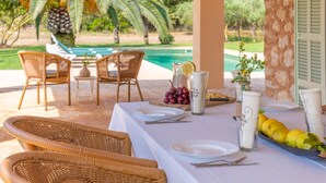 Un espace de restauration en plein air, avec des chaises en osier et une table dressée pour deux, donnant sur une piscine et des palmiers.