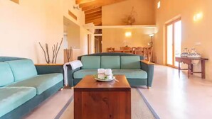 Un salon spacieux avec un canapé vert, une table basse en bois et, au fond, un coin repas.