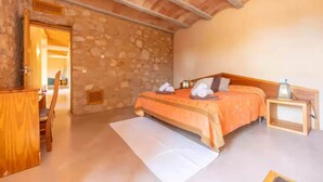 Une chambre avec un mur en pierre, un lit en bois, une table de chevet et un bureau avec une chaise.