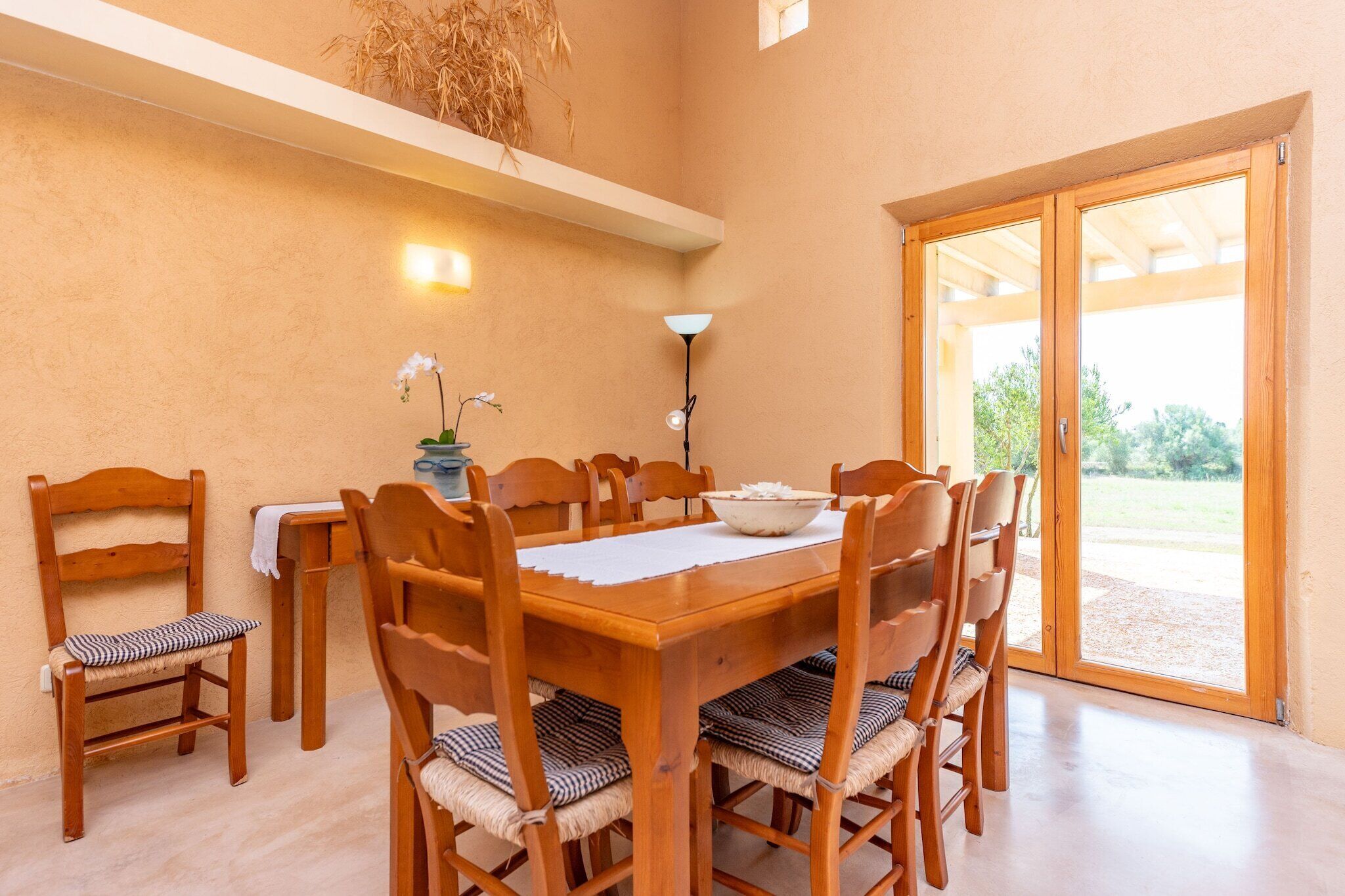Un coin repas avec une table et des chaises en bois, un bol posé sur la table et une vue à travers une porte vitrée.