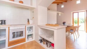 Een moderne keuken met witte kasten, een inbouwoven en een eethoek met een houten tafel en stoelen.