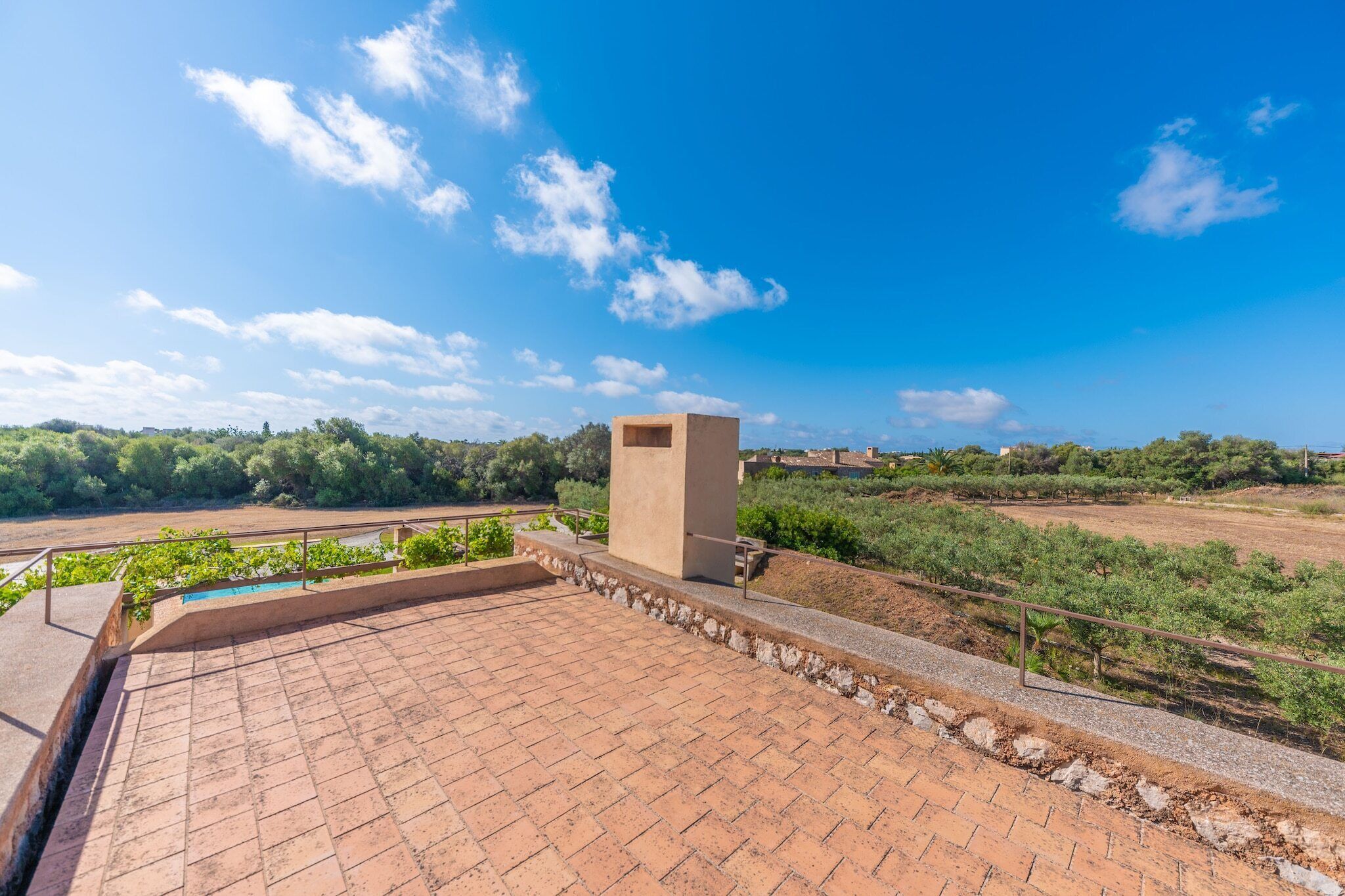 Une terrasse sur le toit, avec un sol en briques, une petite construction de couleur beige et une vue sur un vignoble et des bâtiments éloignés.