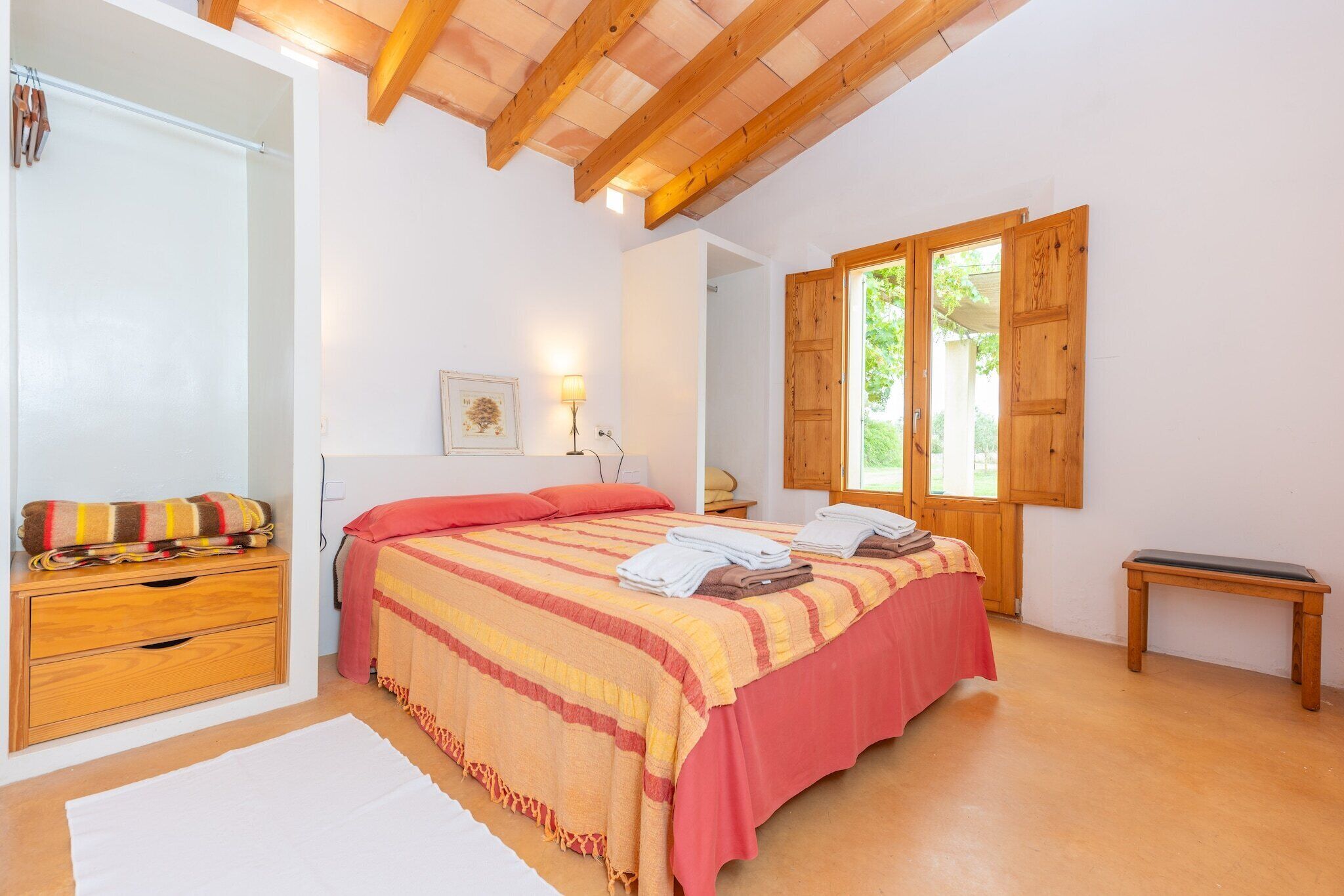 A bedroom with a bed, wooden bench, and a window with wooden shutters.