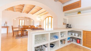 Een ruime keuken met een gewelfde plafond, een eethoek met een houten tafel en stoelen, en inbouwplanken met keukengerei.