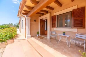 Relax outdoors with a patio featuring a table and chairs, surrounded by lush greenery and a wooden door leading to the interior.