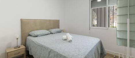 A neatly made bed with a patterned bedspread, a bedside table with a lamp, and a window with a view of the outside.