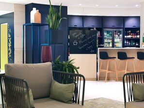 Ein moderner Barbereich mit einer Kreidetafel-Speisekarte, Barhocker und einer Sitzecke inklusive Sofa und Sesseln.
