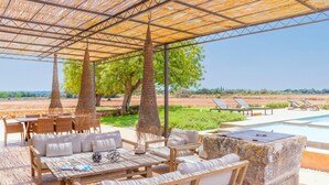 An outdoor seating area with wicker furniture, a stone fire pit, and a view of the pool and landscape. - Son Catxo - Villa With Private Pool In Búger (, Illes Balears)
