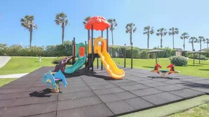 A playground with a yellow slide, a blue horse ride, and a red and yellow climbing structure. - Las Americas - Apartment In Isla Cristina (, Huelva)
