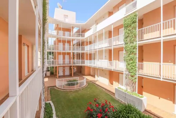 Un patio de varios niveles con balcones, un jardín central y una fachada de edificio con planta trepadora.