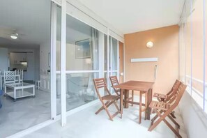 Un espacio de estar moderno con una mesa de comedor de madera y sillas, una puerta corredera de vidrio que da a una cocina, y un ventilador de techo blanco.
