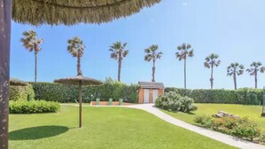 A well-maintained garden with a pathway leading to a small building, surrounded by palm trees and neatly trimmed hedges. - Las Americas - Apartment In Isla Cristina (, Huelva)
