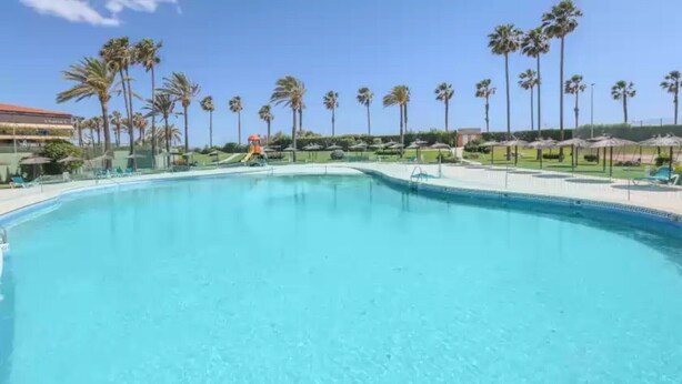 A large, clear swimming pool with palm trees and umbrellas in the background. - Las Americas - Apartment In Isla Cristina (, Huelva)