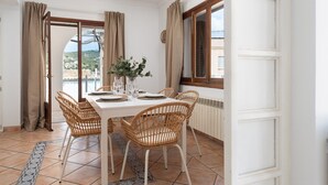 A dining area with a table set for four, wicker chairs, a vase with greenery, and a view through a glass door. - Ca Ne Margalide - Villa With Private Pool (, Illes Balears)
