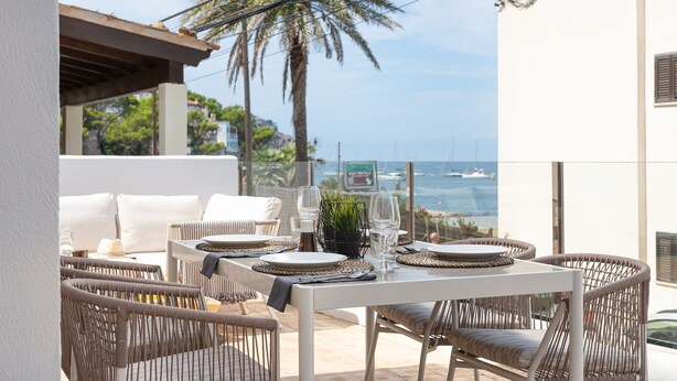 A dining area with wicker chairs, a white table set with plates, glasses, and a small plant. - Ca Ne Margalide - Villa With Private Pool (, Illes Balears)
