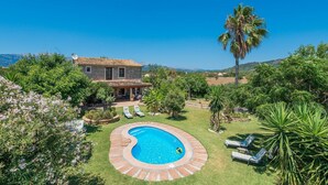 A villa with a swimming pool, surrounded by lush greenery and a clear blue sky.