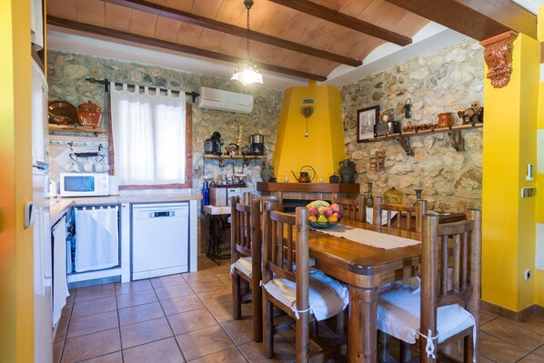 A rustic kitchen with stone walls, wooden beams, and a dining area with a wooden table and chairs.