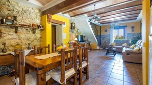 A dining area with a wooden table and chairs, a stone wall, and a staircase leading to another level.