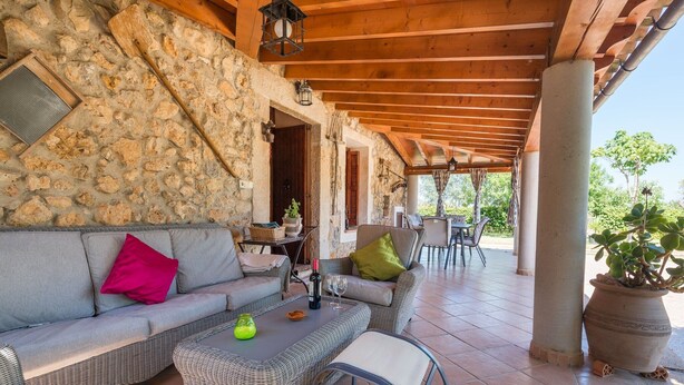 An outdoor patio with wicker furniture, stone walls, and a wooden ceiling.
